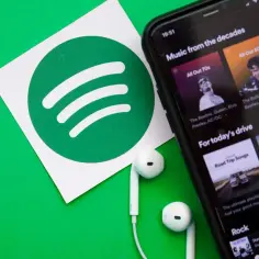 Logo Spotify, smartfon z aplikacją muzyczną i słuchawki na zielonym tle.